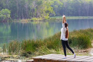 Woman stretching at the pier next to natural lake in the forest for morning exercise and yoga workout routine in peaceful serene environment