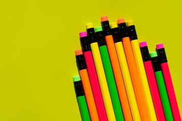 top view of colorful pencils with erasers on green background.