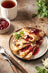 Close up Crepes with raspberry jam and a mint leaf in brown plate. Breakfast composition