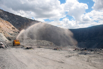 Heavy truck pours the road with water in the iron ore quarry. Dust removal, protection of the environment. Irrigation of the road from dust