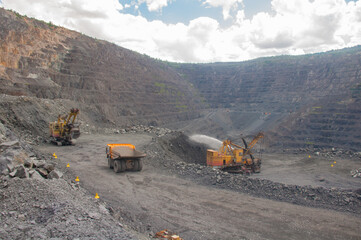 equipment (excavators, dump trucks, drilling rigs) moves along the roads of the iron ore quarry. At the bottom of the quarry, explosives for a technological explosion were laid.