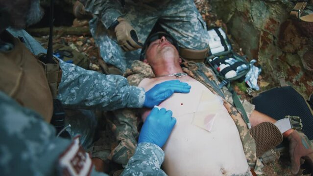 Two medics fixed the bandage with adhesive tape, provides first aid. Soldier lying wounded with punctured lungs. Military concept