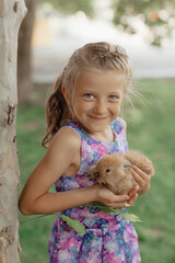 Little girl sitting on the green grass with rabbit. Cute child girl holding a bunny in her hands on Easter day.