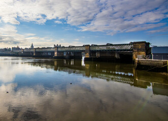 The Rochester Railway Bridge over the River Medway, across the water from the North East bank.  A cold blue sky and a few clouds.  The reflection of the bridge is seen in the river.