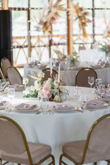 Wedding decor in pink. Banquet tables with tablecloths are decorated with compositions of flowers, on the tables are plates, glasses and candles
