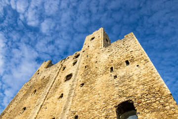 The tower of Rochester Castle, looking up towards the blue sky, with very light clouds.  The sun is shining on the walls.  October 2021.