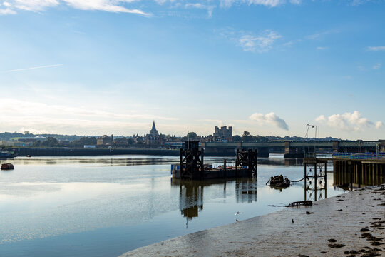 Rochester Castle and Cathedral, from East of the Rochester Bridge, across the Medway River.  A clear autumn day in October 2021. A derelict jetty and dockside equipment are in the river. 