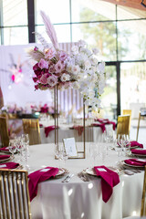 Elegant banquet table set with glasses decorated with gold, lit candles and pink flowers