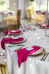 Elegant banquet table set with glasses decorated with gold, lit candles and pink flowers