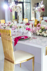Elegant banquet table set with glasses decorated with gold, lit candles and pink flowers