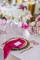 Elegant banquet table set with glasses decorated with gold, lit candles and pink flowers