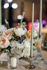 Banquet table is decorated with plates, cutlery, glasses, candles and flower arrangements. Wedding decor