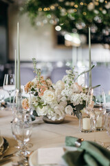 Banquet table is decorated with plates, cutlery, glasses, candles and flower arrangements. Wedding decor