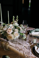 Banquet table is decorated with plates, cutlery, glasses, candles and flower arrangements. Wedding decor
