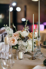 Banquet table is decorated with plates, cutlery, glasses, candles and flower arrangements. Wedding decor