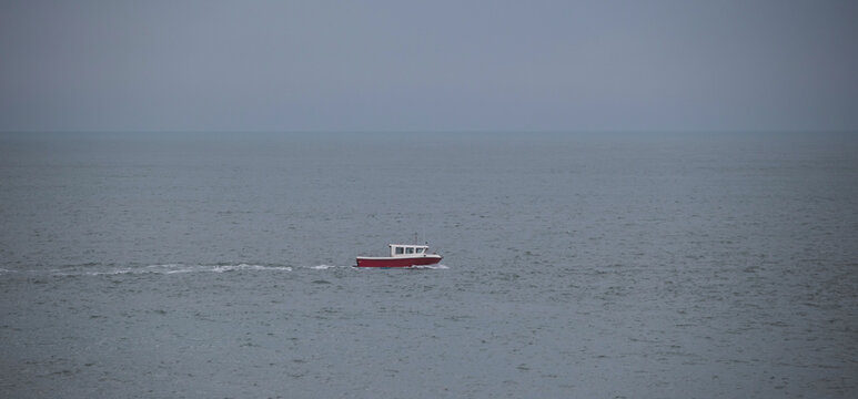 A small, red fishing boat at sea. Foggy sea, cloudy weather shortly before the storm