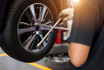 Auto mechanic with electric screwdriver changing tire outside at car service center. Hands replace...