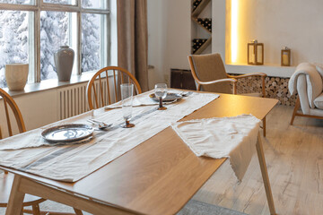 cozy warm home interior of a chic country chalet with a huge panoramic window overlooking the winter forest. open plan, wood decoration, warm colors and a family hearth