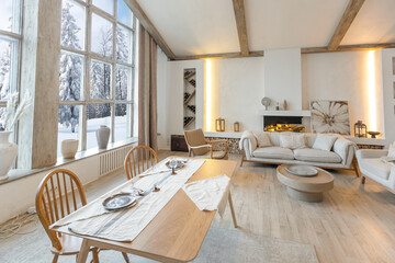 cozy warm home interior of a chic country chalet with a huge panoramic window overlooking the winter forest. open plan, wood decoration, warm colors and a family hearth