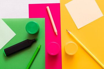 top view of stationery near jars with paint on colorful background.