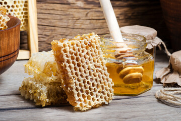 fresh bee Honey in honeycombs and in a glass jar with a honey dipper on a wooden background.