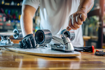 man use the socket tool or hex keys to remove the nuts on skateboard and adjusts suspension in workshop, Skateboard maintenance and repair concept. Selective focus on suspension set