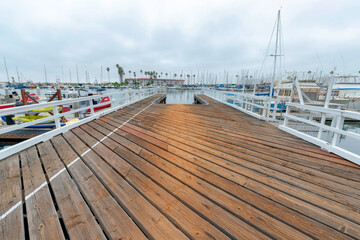 Wood planks flooring on a harbor dock with white fence barrier at Oceanside, California