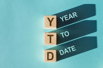 Three wooden cubes with the word YTD - year to date - on them on light blue background with shadows.
