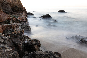 Fototapeta na wymiar Rocky coastline in the early morning at Malibu, California. Silky waves glide over the sand. 
