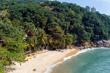 Aerial view of sunny tropical beach with turquoise waves crashing on white sand. Praia do Éden (Eden’s Beach), Guarujá, Brazil. Small beach with jungle-like surroundings