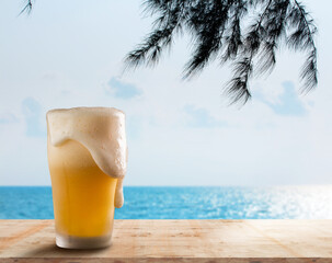 a beer bubble overflowing from a glass of beer lay on a wooden counter by the beach overlooking the...