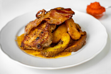 Grilled pork steak with bacon strips, baked potato on white plate, ajvar.
