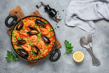 Spanish paella with seafood in a frying pan on a gray concrete background. Top view, flat lay. Mediterranean dish.