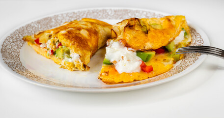 Sliced omelette with avocado, red pepper, linseed, onion and yogurt on plate with fork.