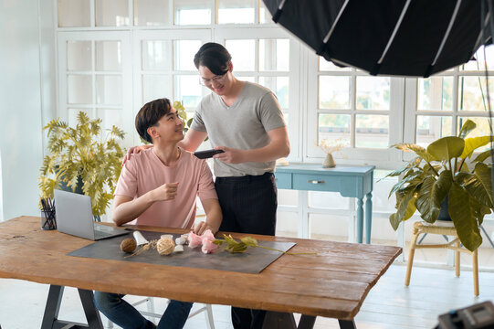 Young smiling gay couple working on new project and shooting pictures of new product by smartphone