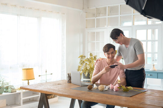 Young smiling gay couple working on new project and shooting pictures of new product by smartphone