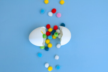 Eggshell and a path of multi-colored pompoms on a blue background, focus on the shell