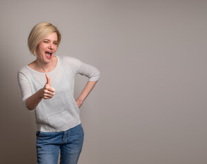 Young attractive woman winking and showing thumb up on a gray background