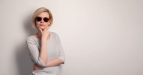 Portrait of a beautiful young girl with sunglasses touching chin on a gray background