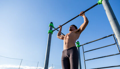 Strong guy doing pull up in a calisthenics park. Outdoor training and working out.