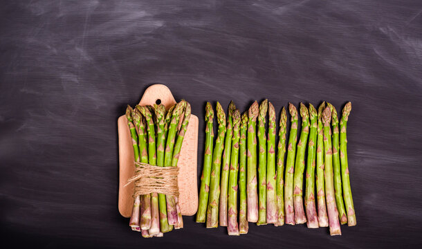 A bunch of fresh asparagus on a cutting board and a stem of a black chalk board.