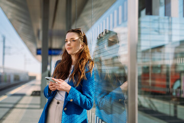 Young woman waiting at rail station. Holding smartphone and waiting for her train. Public transport.