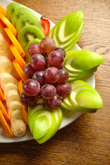 Fresh raw organic summer berries and exotic fruits in a white plate on the background of a table and a tree.