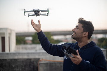 young indian male catching launching folding drone with camera from hand with controller in other hand smiling showing the rise of manufacturing and technology