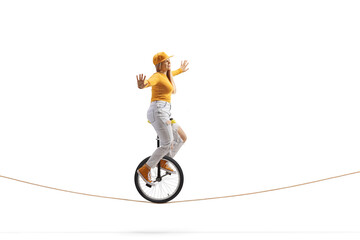 Full length side shot of a young female riding a unicycle on a tightrope