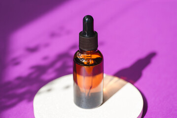 Amber glass dropper bottle with black lid on a podium with plants shadows on purple background.