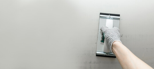 Plaster float in male hand in glove against a gray wall. Plastering grater in the hands of a worker. Banner