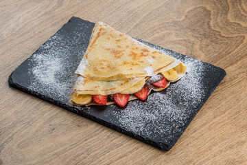 Pancake with strawberry and banana on a black tray
