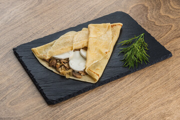 Pancake with mushrooms on a black tray