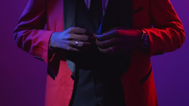 Man fashion. Gentleman style. Luxury party look. Neon light unrecognizable confident guy buttoning red elegant tuxedo suit isolated on fluorescent purple.